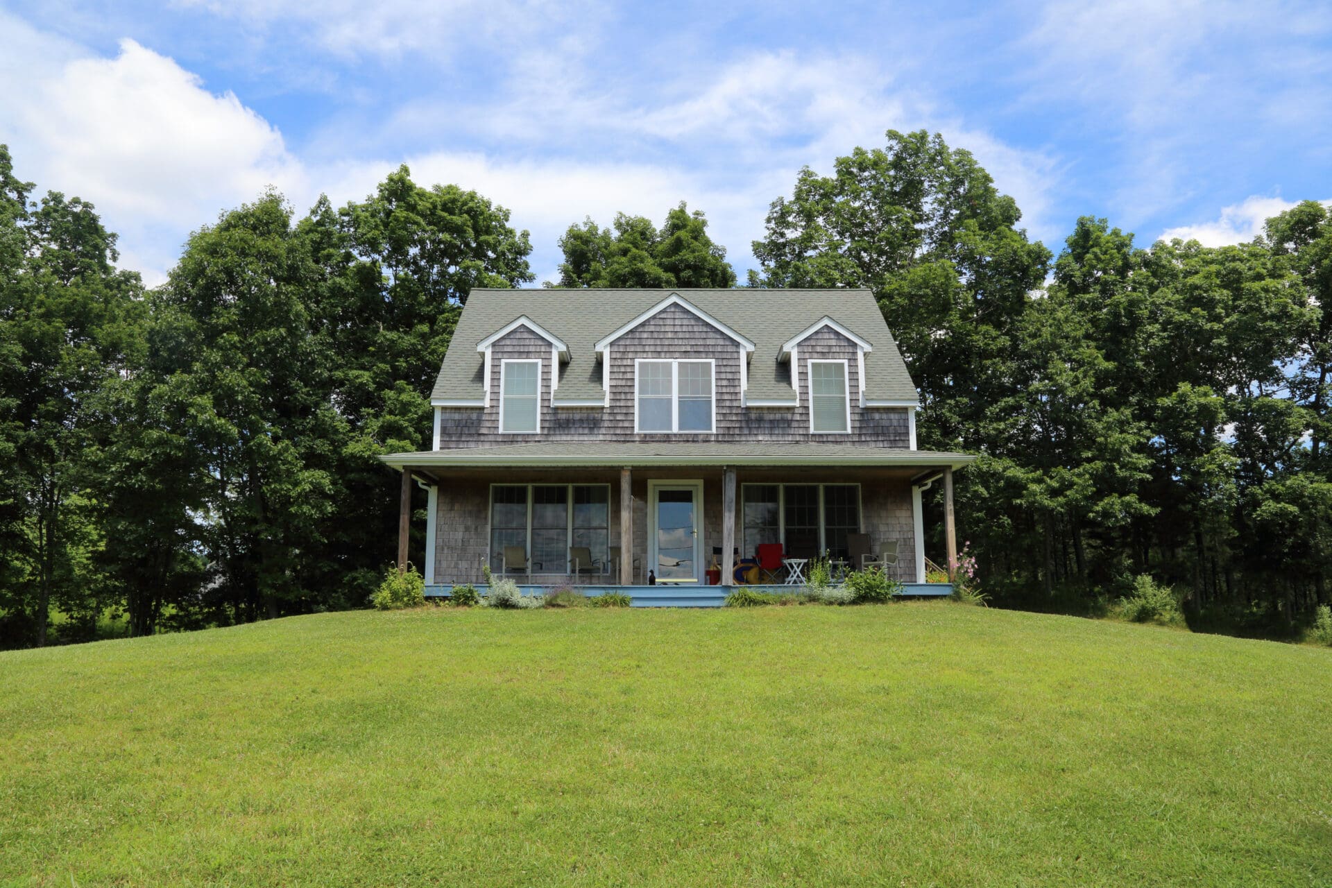 Gray shingled house on grassy hill.